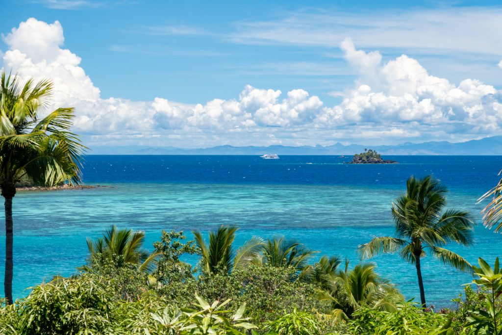 Sunny day, the view from the tropical island with cruise ship in the background - Leisure Travel Enterprises 