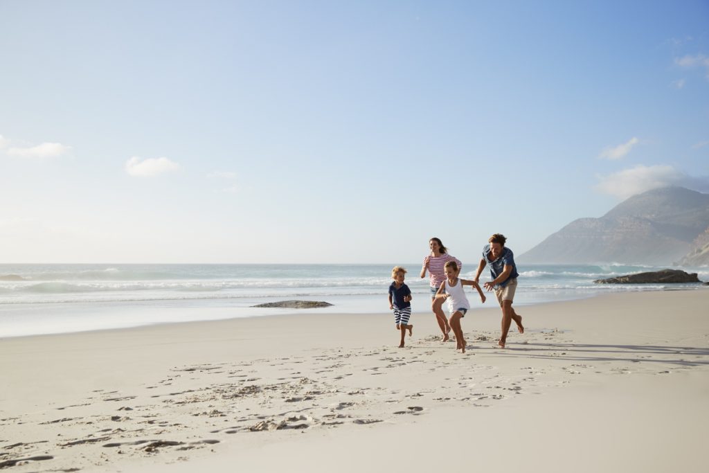 Parents Running Along Beach With Children On Summer Vacation - Leisure Travel Enterprises 