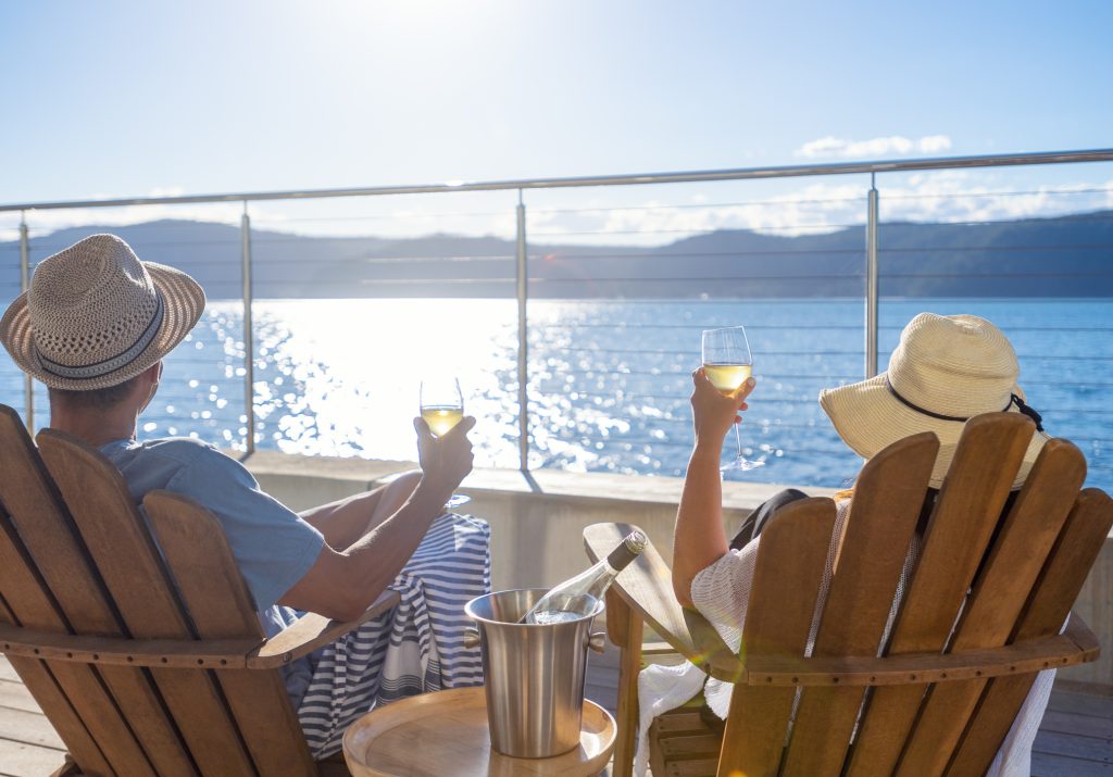 Couple relaxing and drinking wine on deck chairs in an over water bungalow - LTE